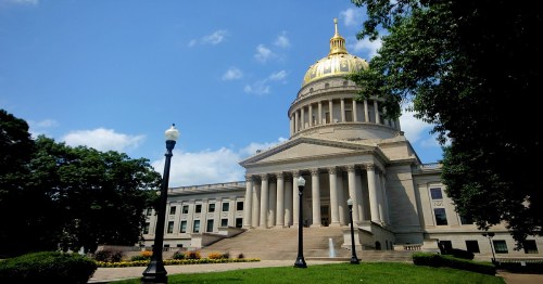 West Virginia State Capitol building with a golden dome, surrounded by green lawns and trees under a blue sky.