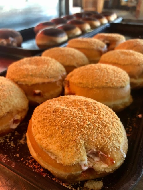 A tray of freshly made donuts coated in crumbs, with some filled with cream and fruit filling.