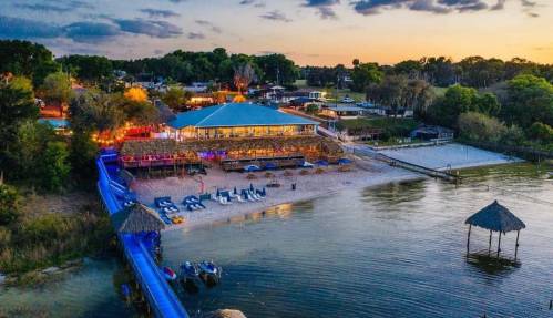 Aerial view of a beachside venue with a blue roof, sandy area, and boats near the water at sunset.