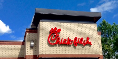 Signage of a Chick-fil-A restaurant against a blue sky with clouds.