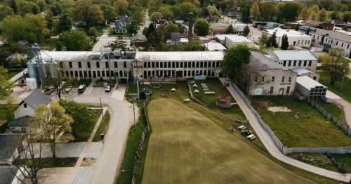 Aerial view of a historic building complex surrounded by greenery and a lawn, with nearby residential areas.