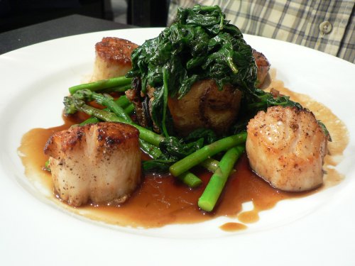 A plate featuring seared scallops, sautéed greens, and asparagus drizzled with a savory sauce.