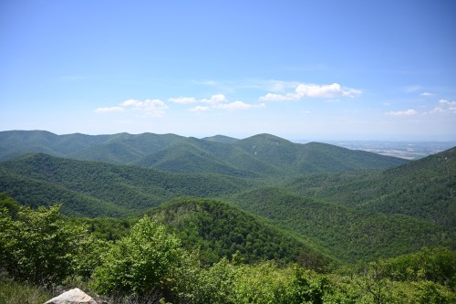 Lush green mountains under a clear blue sky, with rolling hills and distant valleys visible in the background.