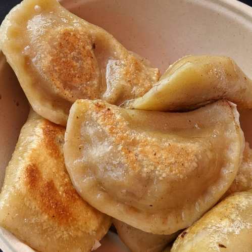 A close-up of golden-brown dumplings, lightly crispy on one side, served in a bowl.