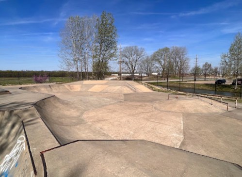 A wide view of a skatepark with smooth concrete ramps and a clear blue sky in the background.