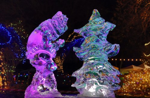 Two colorful ice sculptures: a bear and a Christmas tree, illuminated by vibrant lights in a festive setting.
