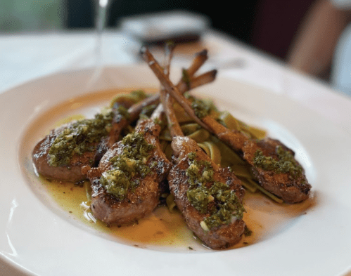 A plate of grilled lamb chops topped with herb sauce, served on a bed of pasta.