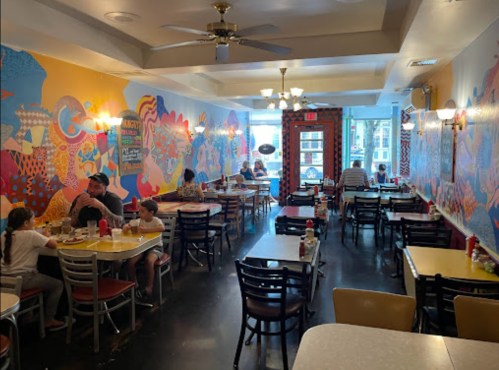 Colorful restaurant interior with vibrant murals, tables occupied by diners, and a bright, welcoming atmosphere.
