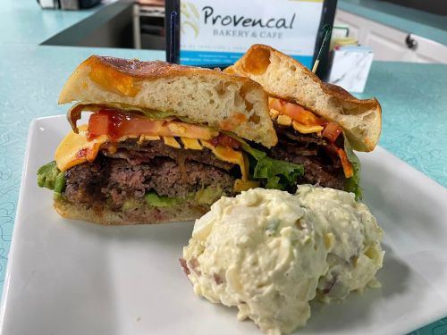 A close-up of a hearty sandwich with layers of meat, cheese, lettuce, and tomato, served with a side of potato salad.
