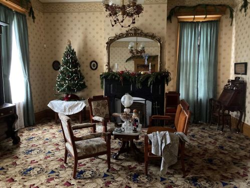 A cozy room decorated for the holidays, featuring a Christmas tree, fireplace, and vintage furniture.