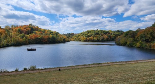 A serene lake surrounded by colorful autumn trees under a partly cloudy sky.