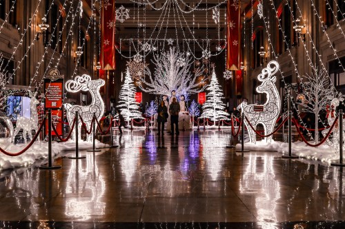A festive indoor scene with illuminated reindeer, trees, and decorations, reflecting on a polished floor.