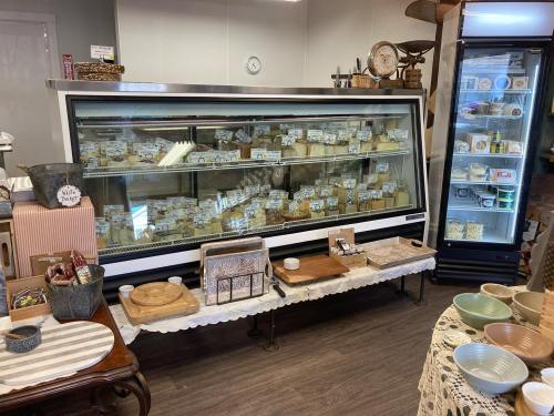 A display case filled with various cheeses, surrounded by wooden serving boards and colorful bowls in a cozy shop.