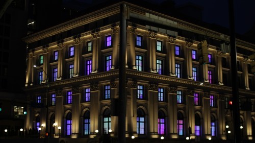 A historic building illuminated at night with colorful lights shining through its windows.