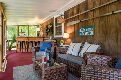 Cozy porch with wicker furniture, a bar, and decor featuring a water theme, surrounded by greenery.