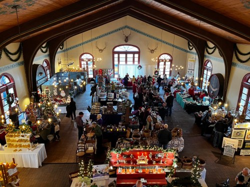 A bustling holiday market inside a large, decorated hall with vendors and shoppers among festive displays.