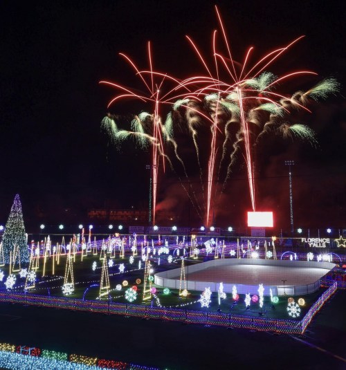 Colorful fireworks illuminate a festive ice skating rink surrounded by holiday lights and decorations.