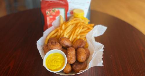 A basket of golden fries and fried snacks with a cup of mustard and ketchup on a wooden table.