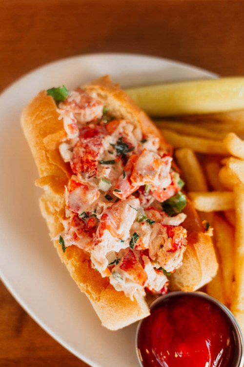 A lobster roll filled with lobster meat and herbs, served with fries and a side of ketchup.