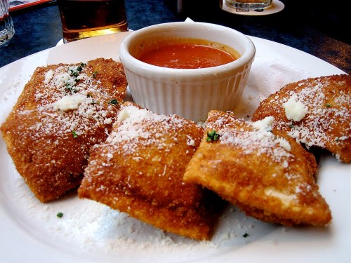 A plate of golden-brown fried ravioli served with marinara sauce and sprinkled with cheese.