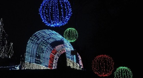 Colorful holiday lights form an illuminated arch and large decorative orbs against a dark night sky.