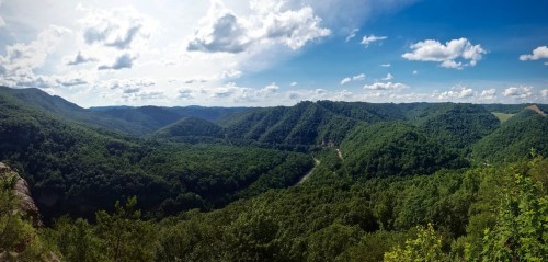 A panoramic view of lush green mountains and valleys under a bright blue sky with scattered clouds.