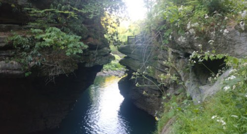 A serene river flows between rocky cliffs, surrounded by lush greenery and trees.