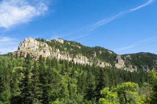 A scenic view of a rocky mountain range surrounded by lush green trees under a clear blue sky.