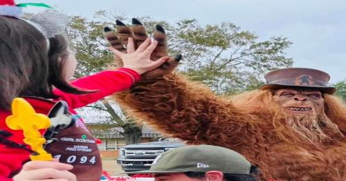 A person in a furry bear costume with a top hat interacts playfully with a child, both reaching out their hands.