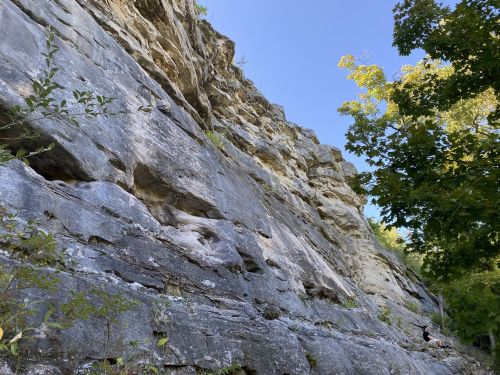 A rocky cliffside with greenery at the base and a clear blue sky above.