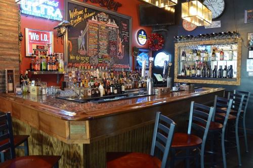 A cozy bar with a wooden counter, shelves of drinks, and a chalkboard menu in a vibrant setting.