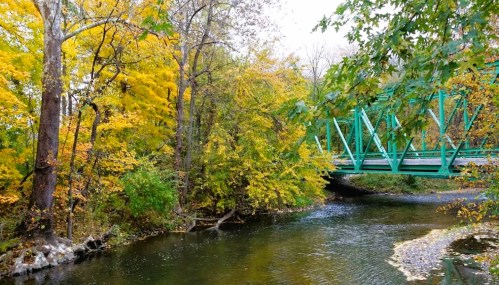 A serene river scene with vibrant autumn foliage and a green bridge crossing over the water.