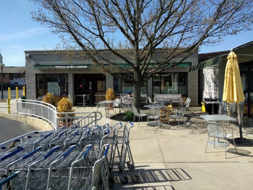 Exterior view of Whole Earth Center with shopping carts in foreground, a tree, and outdoor seating area.