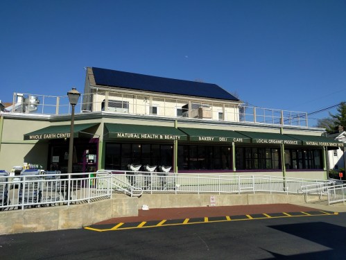 A storefront of Whole Earth Center featuring a bakery, deli, and organic produce, with solar panels on the roof.