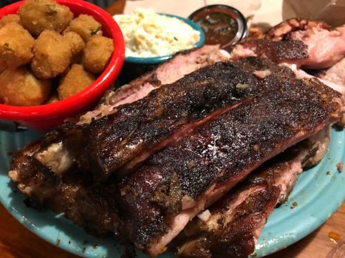A plate of grilled ribs with sides of coleslaw, fried okra, and barbecue sauce.