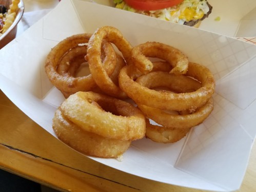 A serving of crispy, golden-brown onion rings in a paper tray.
