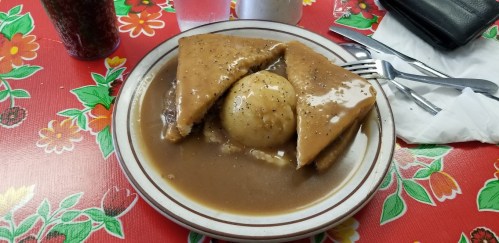 A plate of food featuring two triangular pieces of bread and a round dumpling in a brown sauce, on a floral tablecloth.
