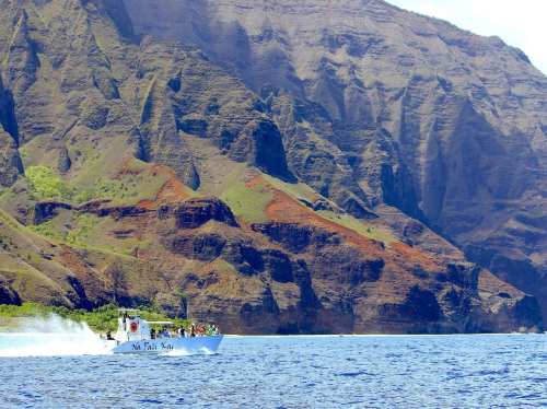 A boat navigates blue waters near steep, colorful cliffs under a clear sky.