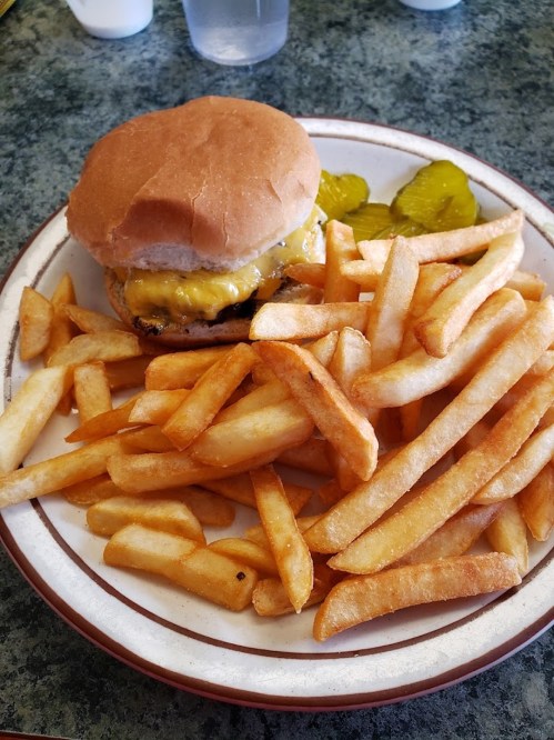 A plate with a cheeseburger on a bun, accompanied by a generous serving of golden French fries and pickles.