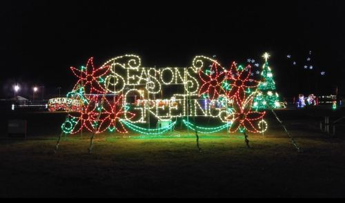 Colorful holiday lights display featuring "Season's Greetings" with flowers and a decorated Christmas tree in the background.