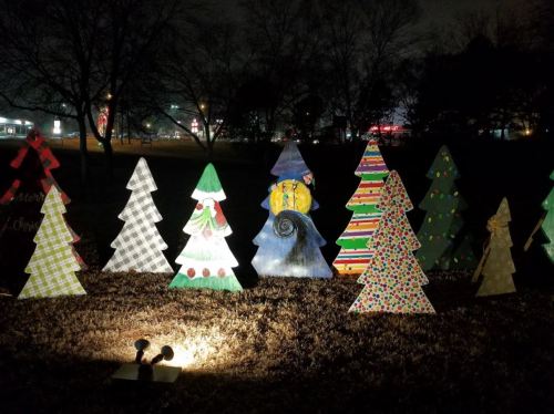 Colorful, decorated wooden Christmas trees illuminated at night in a festive outdoor display.