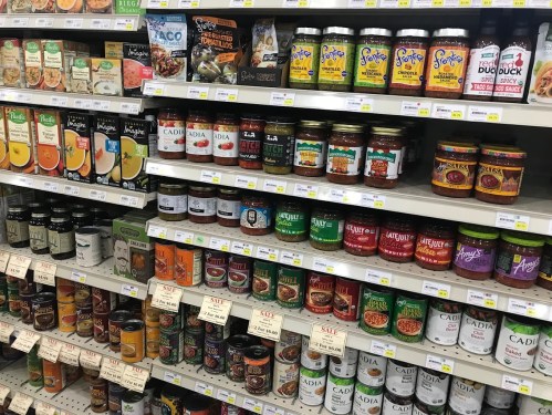 A grocery store shelf filled with various jars and cans of sauces, spreads, and canned goods, all neatly organized.