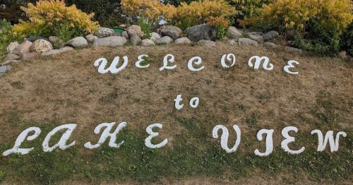 A grassy area with a stone border featuring a sign that reads "Welcome to Lake View" in white letters.