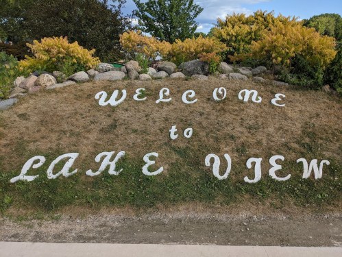 Sign reading "Welcome to Lake View" on a grassy area with rocks and trees in the background.
