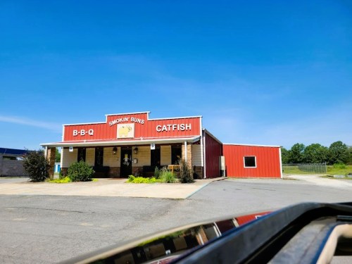 A red and beige restaurant building with a sign reading "Smokin' Buns BBQ Catfish" under a clear blue sky.