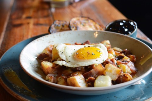 A bowl of crispy potatoes topped with a sunny-side-up egg, served with a side of jam and toasted bread.