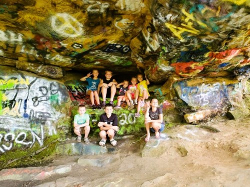 A group of eight children sitting in a colorful, graffiti-covered cave.