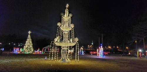 A festive park scene at night featuring a large illuminated fountain and a decorated Christmas tree.