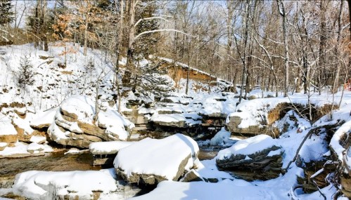 A serene winter landscape featuring a snow-covered creek surrounded by trees and rocky formations.