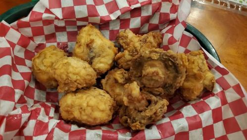 A basket lined with red and white checkered paper filled with crispy fried chicken and fried mushrooms.